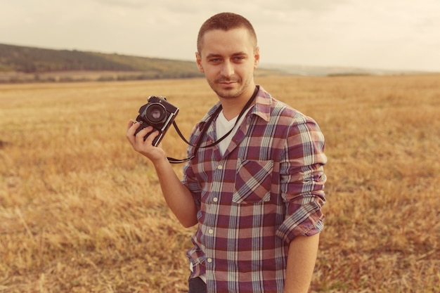 Retrato de atractivo fotógrafo masculino al aire libre al atardecer. Joven con una cámara en mano