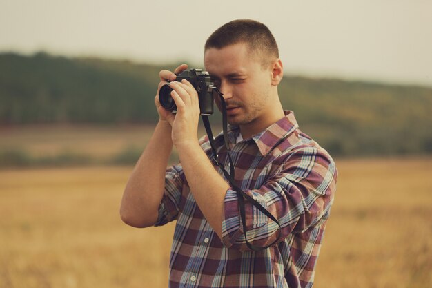 Retrato de atractivo fotógrafo masculino al aire libre al atardecer. Joven con una cámara en mano