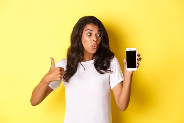Retrato de atractivo modelo femenino afroamericano que recomienda una aplicación que muestra el teléfono móvil