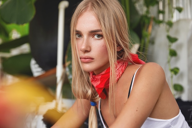 Retrato de atractivo modelo de mujer joven relajada con pañuelo rojo en el cuello, tiene su propio estilo, se sienta contra el acogedor interior del café