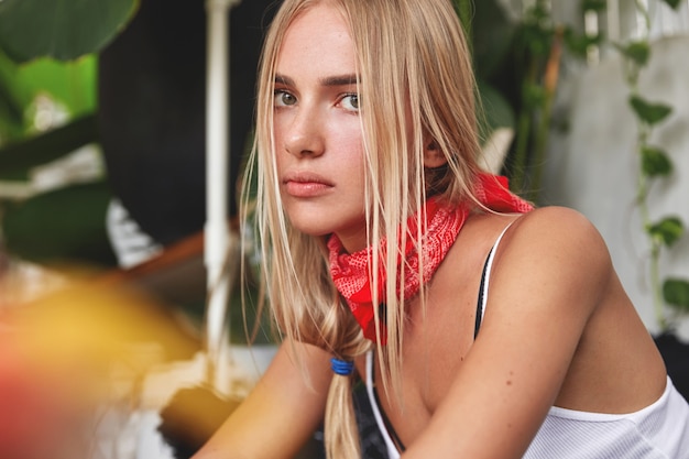 Retrato de atractivo modelo de mujer joven relajada con pañuelo rojo en el cuello, tiene su propio estilo, se sienta contra el acogedor interior del café