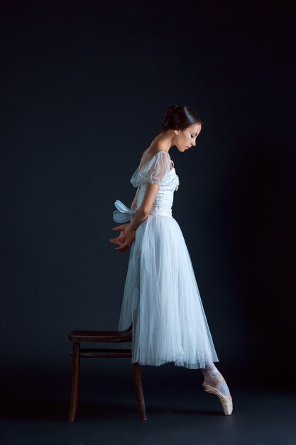 Retrato de la bailarina clásica en vestido blanco sobre pared negra