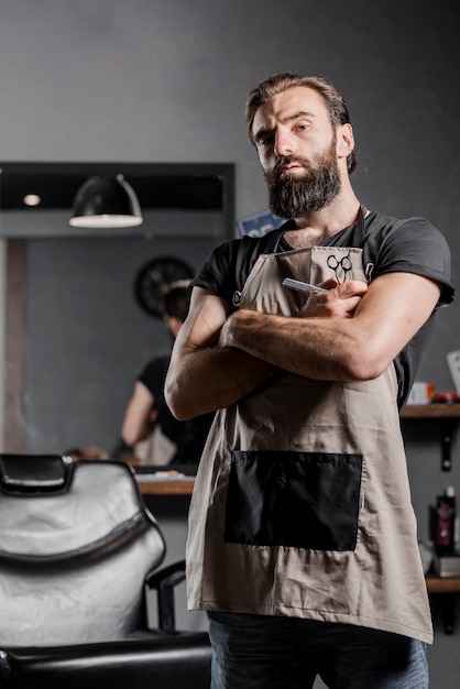 Retrato de un barbero barbudo masculino mediados de adulto con los brazos cruzados