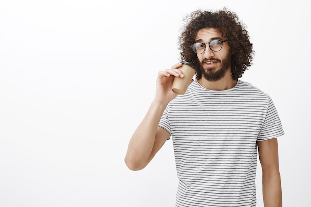 Retrato de barista masculino delgado guapo seguro en camiseta de moda y gafas, tomando café de la taza y mirando