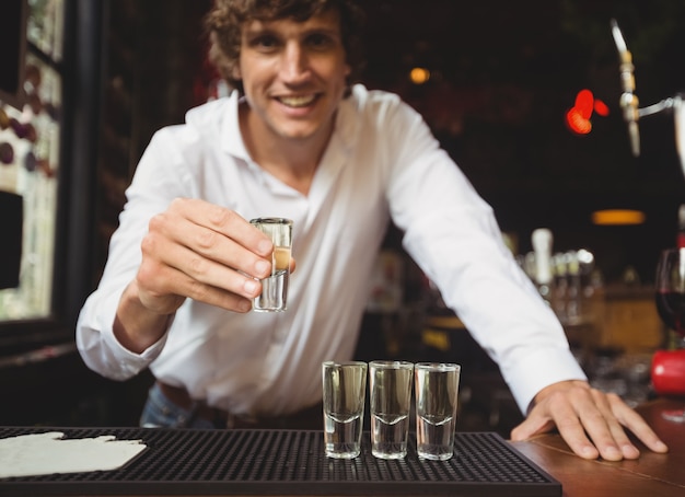 Retrato de barman con vaso de chupito de tequila en barra de bar