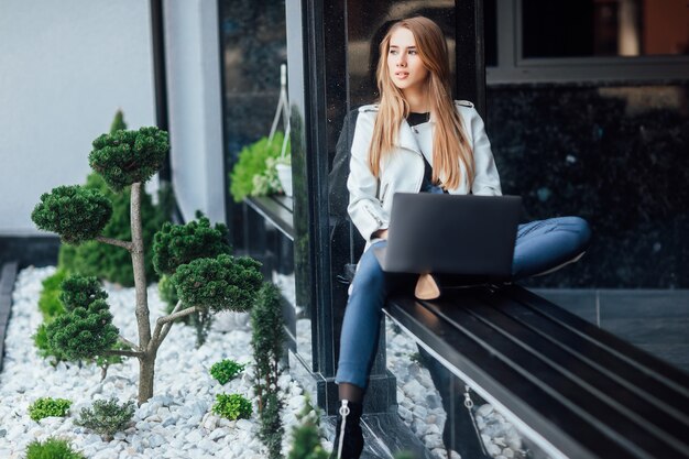 Retrato bastante empresaria en ropa fasion en escaleras al aire libre. Ella usa una computadora portátil, con ganas también.