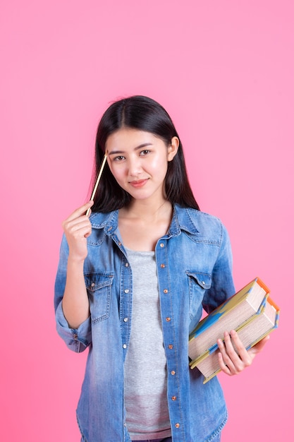 Retrato bastante hembra adolescente sosteniendo libros en su brazo y usando lápiz en rosa