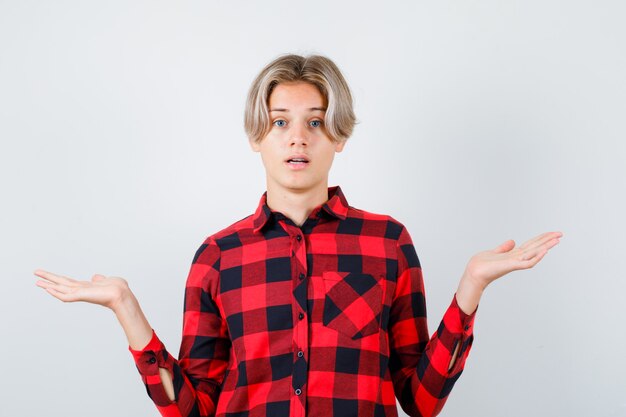 Retrato de bastante jovencito mostrando gesto de impotencia en camisa a cuadros y mirando desconcertado vista frontal