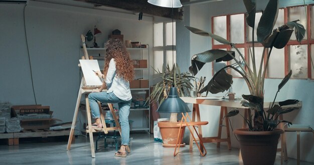 Retrato de una bella artista de pelo largo trabajando en su lienzo en un estudio