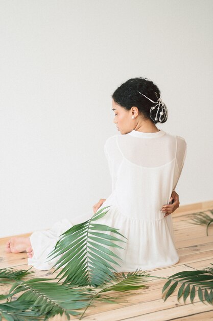 Retrato de bella dama en la habitación vacía sentada en vestido blanco largo