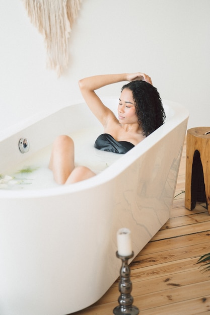 Retrato de bella dama en la habitación vacía tomando un baño de leche y pensando sosteniendo su cabello