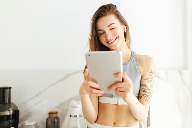 Retrato de una bella dama sonriente en una parte superior deportiva de pie con una computadora portátil en la mano y auriculares