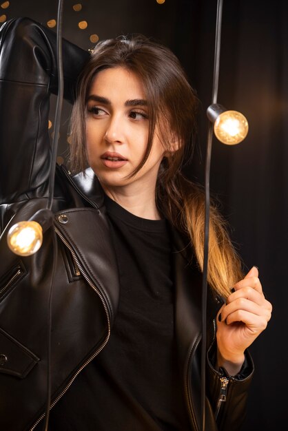 Retrato de una bella joven modelo en chaqueta de cuero negro posando junto a las lámparas.