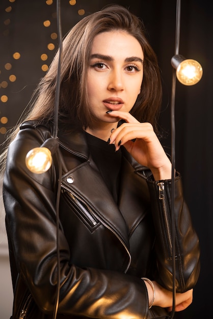 Retrato de una bella joven modelo en chaqueta de cuero negro posando junto a las lámparas.