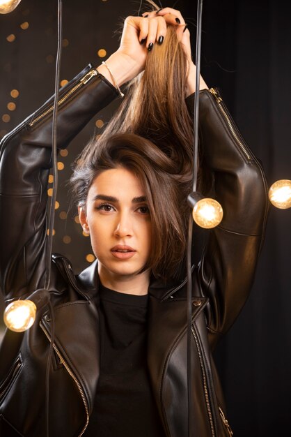 Retrato de una bella joven modelo en chaqueta de cuero negro posando junto a las lámparas.
