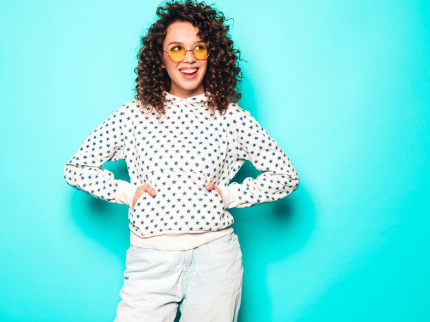 Retrato de la bella modelo sonriente con peinado afro rizos vestido con ropa hipster de verano. Mujer divertida y positiva de moda con capucha blanca