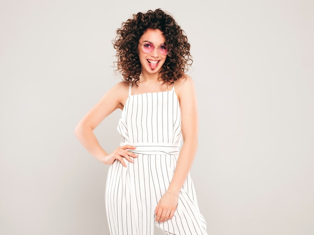 Retrato de bella modelo sonriente con peinado afro rizos vestido con ropa hipster de verano. Mujer divertida y positiva de moda muestra lengua