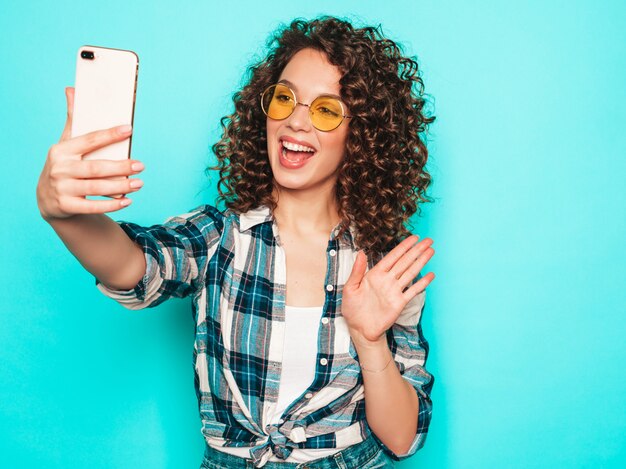 Retrato de la bella modelo sonriente con peinado afro rizos vestido con ropa hipster de verano.La mujer de moda divertida y positiva hace selfie
