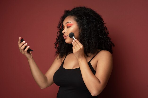 Retrato de una bella mujer aplicando maquillaje en su rostro mientras se mira en el espejo