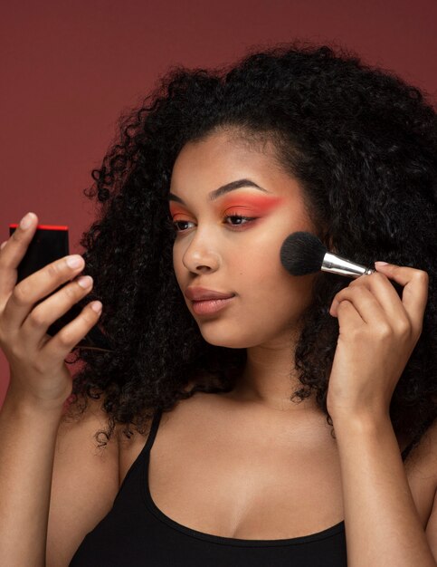 Retrato de una bella mujer aplicando maquillaje en su rostro mientras se mira en el espejo