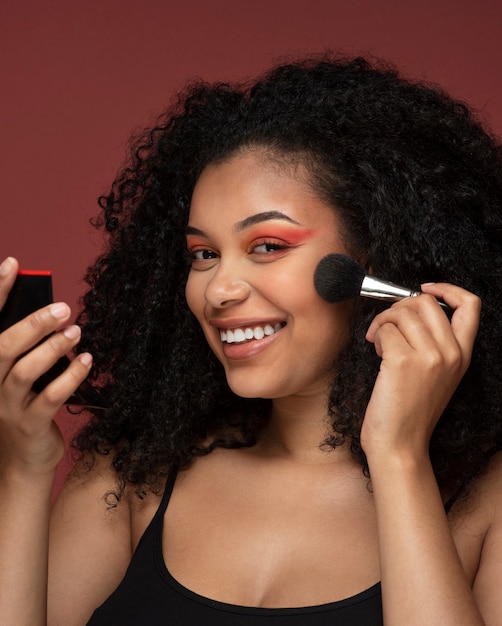 Retrato de una bella mujer aplicando maquillaje en su rostro mientras se mira en el espejo