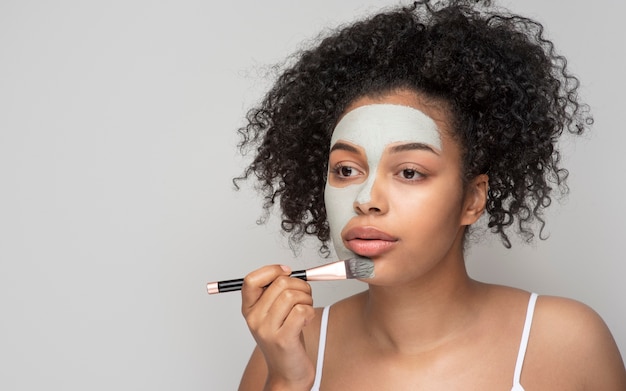 Retrato de una bella mujer aplicando mascarilla con un pincel de maquillaje en el rostro