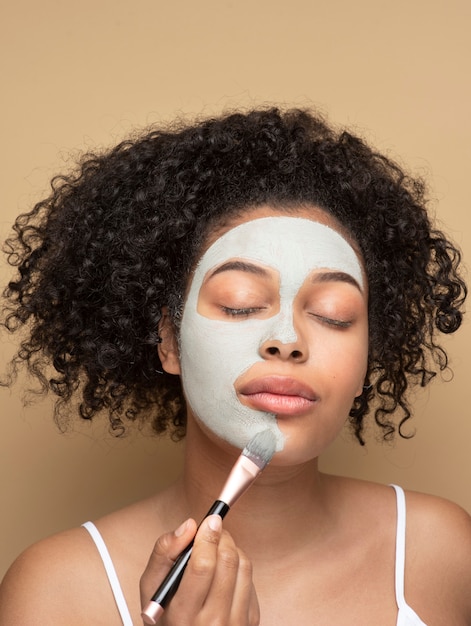 Retrato de una bella mujer aplicando mascarilla con un pincel de maquillaje en el rostro