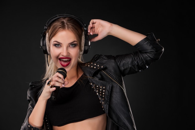 Retrato de una bella mujer cantando en el micrófono con auriculares en estudio sobre fondo negro