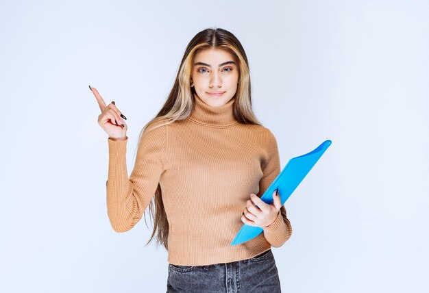 Retrato de una bella mujer con una carpeta de pie y apuntando hacia afuera.