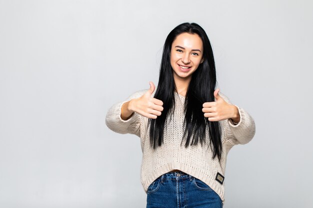 Retrato de una bella mujer joven que muestra los pulgares arriba signo aislado en la pared blanca