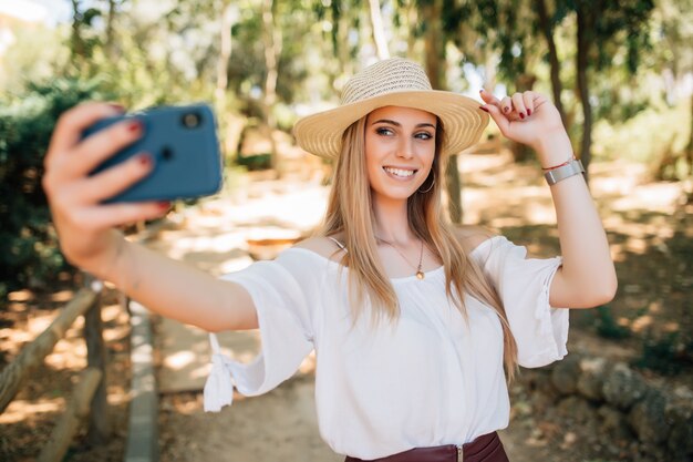 Retrato de una bella mujer joven selfie en el parque con un teléfono inteligente