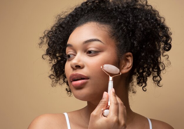 Retrato de una bella mujer masajeando su rostro con un rodillo de masaje