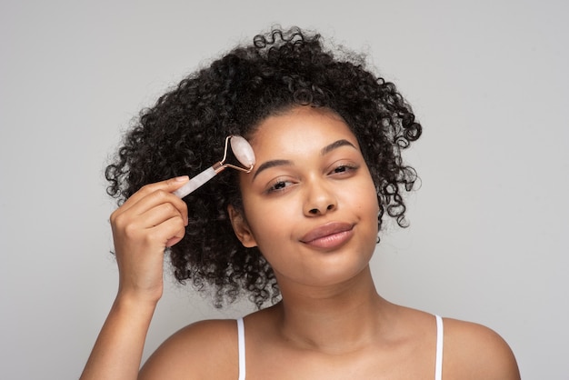 Retrato de una bella mujer masajeando su rostro con un rodillo de masaje