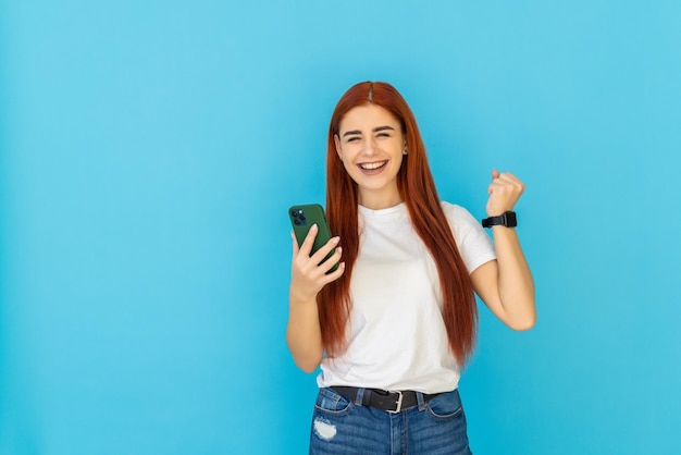 Retrato de una bella mujer mirando el teléfono móvil y celebrando en azul