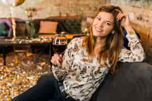 Foto gratuita retrato de una bella mujer sonriente con copa de vino sentado en el sofá