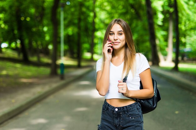 Retrato de una bella mujer sonriente hablando por teléfono en el parque de verano