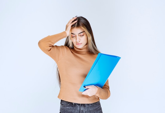 Retrato de una bella mujer sosteniendo una carpeta y posando contra la pared blanca.