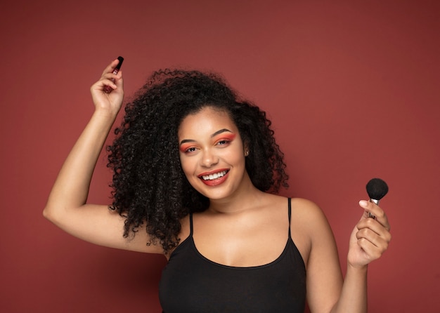 Retrato de una bella mujer sosteniendo lápiz labial y pincel de maquillaje