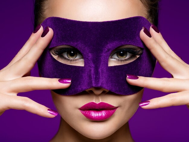 Retrato de una bella mujer con uñas moradas y máscara de teatro violeta en la cara.