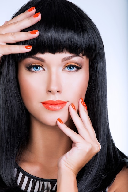 Retrato de una bella mujer con uñas rojas y maquillaje glamour y largos pelos negros