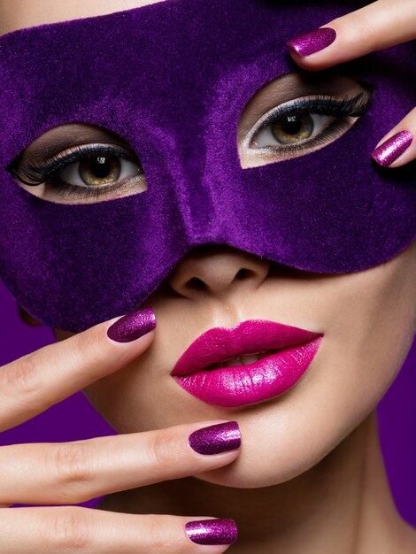 Foto gratuita retrato de una bella mujer con uñas violetas y máscara de teatro en la cara.