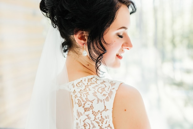 Retrato de una bella novia feliz frente a una ventana. Preparaciones de la boda.