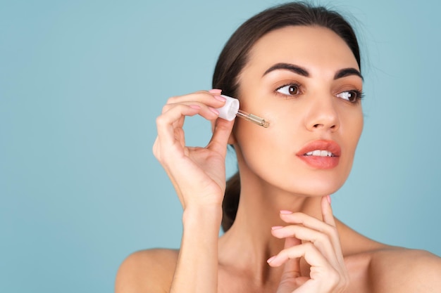 Retrato de belleza cercana de mujer en topless con piel perfecta y maquillaje natural, contiene suero para la juventud e hidratación de la piel, gotero con aceite cosmético