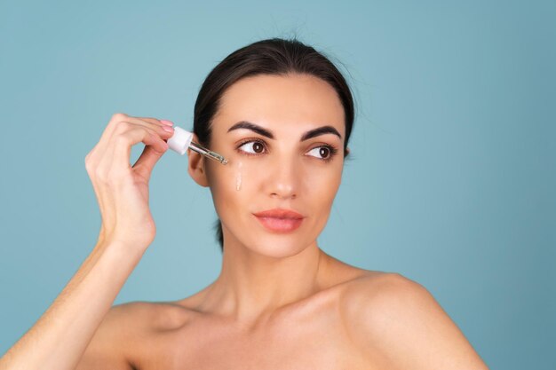 Retrato de belleza cercana de mujer en topless con piel perfecta y maquillaje natural, contiene suero para la juventud e hidratación de la piel, gotero con aceite cosmético