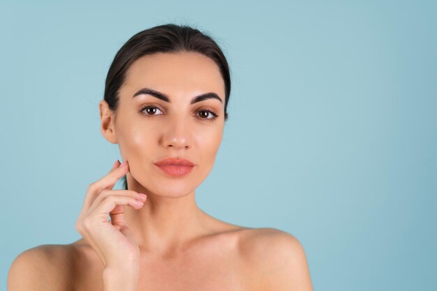 Retrato de belleza cercana de una mujer en topless con piel perfecta y maquillaje natural, labios desnudos regordetes, sobre un fondo azul