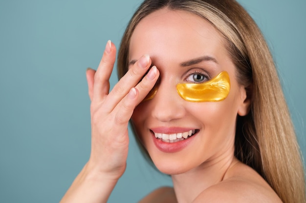 Retrato de belleza cercano de una mujer en topless con piel perfecta y maquillaje natural, parches dorados brillantes debajo de los ojos, para hidratar la piel y aliviar la hinchazón de la cara