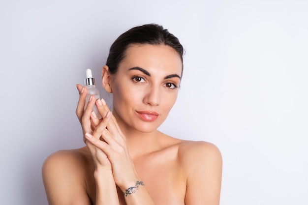 Retrato de belleza cercano de mujer en topless con piel perfecta y maquillaje natural que contiene suero para jóvenes y cuentagotas de hidratación de la piel con aceite cosméticox9