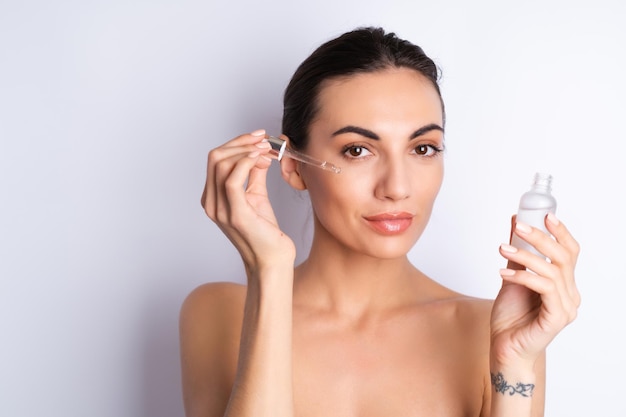 Retrato de belleza cercano de mujer en topless con piel perfecta y maquillaje natural que contiene suero para jóvenes y cuentagotas de hidratación de la piel con aceite cosméticox9