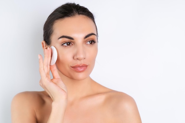 Retrato de belleza cercano de una mujer en topless con piel perfecta y maquillaje natural quitando almohadillas de algodón sobre un fondo blancox9