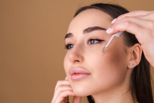 Retrato de belleza cercano de mujer en topless con piel perfecta y maquillaje natural, sostiene suero para la juventud y la hidratación de la piel, cuentagotas con aceite cosmético.